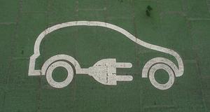 White outline of a car with an electric plug painted on green pavement to mark electric vehicle charging.