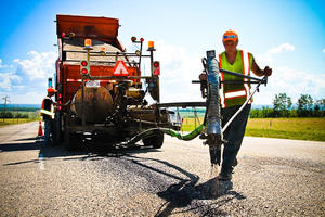 Workers using machinery to apply a seal coat to cracks in asphalt pavement.