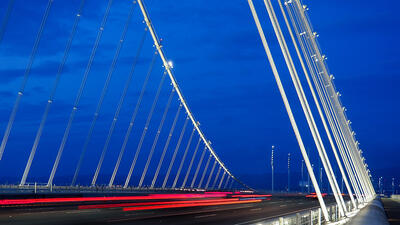 Blurred red tail lights on an illuminated Easter Span of the Bay Bridge at night.